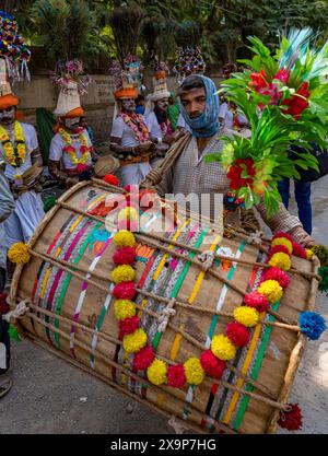 L'uomo mascherato suona un grande tamburo colorato in una processione festosa, circondato da persone in abbigliamento tradizionale Foto Stock