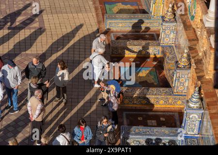 Siviglia, Andalusia, Spagna - 24 ottobre 2023: Gruppo di turisti in Plaza de Espana alcove piastrellate e panchine che rappresentano le province della Spagna, vista da Foto Stock