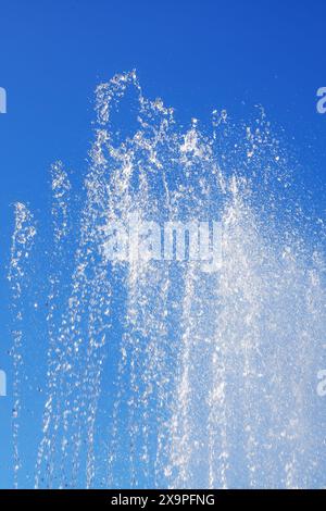 Una fontana liquida che spruzza acqua contro un cielo blu elettrico, creando uno splendido paesaggio naturale con alberi e nuvole sullo sfondo Foto Stock