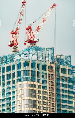 Teleobiettivo di due gru rosse e bianche in cima a un alto edificio di uffici in costruzione a Roppongi a Tokyo. Sfondo nuvola grigia sovradimensionato. Foto Stock