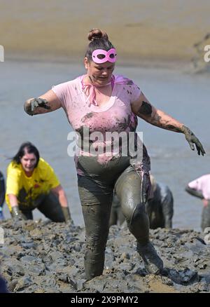 Maldon Essex UK 2 giugno 2024. Centinaia di concorrenti partecipano alla gara del 50° anniversario di Maldon Mud. La gara si svolge su un percorso di 450 metri attraverso il fiume Blackmore da un punto nel Towns Promenade Park e può svolgersi solo con la bassa marea. Questo evento ebbe origine negli anni '70, quando un uomo locale fu sfidato a indossare un smoking per servire un pasto sulla riva del fiume. Ciò ha portato in seguito a una corsa attraverso il fiume dove la gente del posto ha dovuto bere una pinta da un barile di birra in attesa prima di tornare indietro. Ora i concorrenti indossano costumi stravaganti per partecipare allo spettacolo annuale. Credito: Martin Dalt Foto Stock
