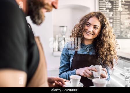Due giovani baristi che lavorano in caffetteria, in piedi al banco. Lavoro di squadra. Foto Stock