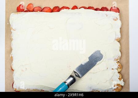 Spalmare la panna sui biscotti savoiardi con una spatola. Prepara la torta tiramisù a casa. Foto Stock