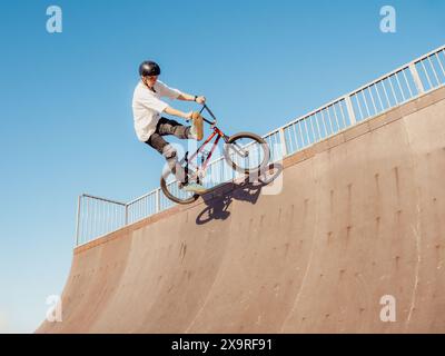 BMX ciclista che vola e fa acrobazie in barattolo in legno. Abile atleta freestyler BMX che salta e fa il CAN-CAN di trick aereo nel parco di rampa in legno Foto Stock