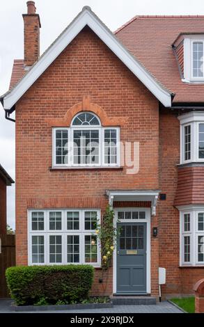 Vista frontale esterna della casa residenziale edoardiana in mattoni rossi nel sobborgo nord di Londra, con porta dipinta di grigio, baldacchino in legno e rose da arrampicata gialle. Foto Stock