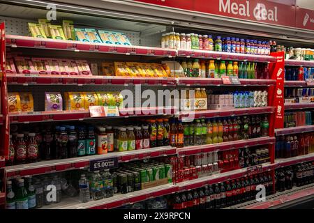 Scaffali completi di varie bevande e succhi di frutta in un supermercato con cartellini dei prezzi e cartelloni per i pasti Foto Stock