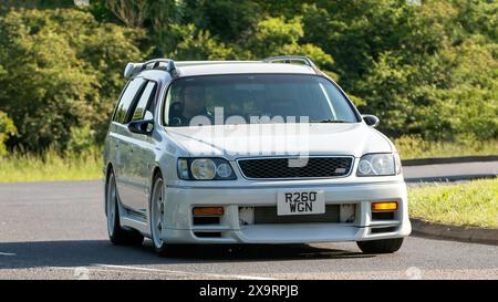 Stony Stratford, Regno Unito - 2 giugno 2024:1998 Nissan Stagea bianca che guida su una strada di campagna britannica Foto Stock