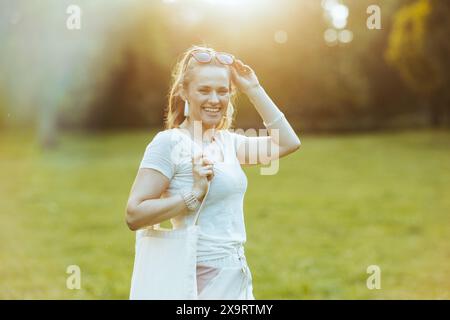 Ora legale. felice donna alla moda 40 anni in camicia bianca con borsa tote nel prato all'aperto nella natura. Foto Stock