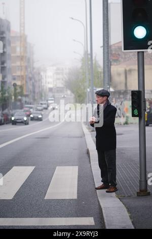 Un elegante uomo di mezza età in piedi di fronte a un passaggio pedonale, che controlla l'ora sul suo orologio da polso. Foto Stock