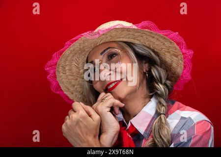 Bella donna che indossa un cappello di paglia con abbigliamento tipico per il festival di Sao Joao, posa e danza. Isolato su sfondo rosso. Foto Stock