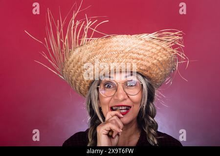 Ritratto in faccia di una bella donna con capelli intrecciati che indossano un cappello di paglia e mangiano arachidi bollite. Celebrazione della festa di San Giovanni. Isolato su SM Foto Stock