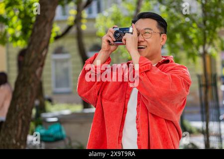 Uomo asiatico di mezza età turista che viaggia nei fine settimana esplorando la città, facendo foto con una macchina fotografica d'epoca retrò all'aperto. Un ragazzo cinese maturo in città. Orizzontale. Stili di vita Foto Stock