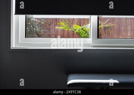 finestra con oscuramento a metà strada che rivela il cortile tropicale esterno e interni minimalisti, ripresa a profondità di campo ridotta, Foto Stock