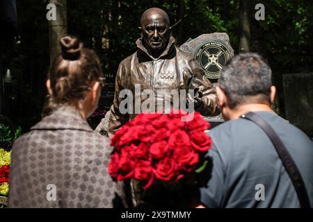 La gente si trova con un mazzo di rose vicino a una scultura del leader mercenario russo Evgenij Prigozhin installata sulla sua tomba durante le celebrazioni del suo compleanno per onorare la sua memoria al cimitero Porokhovskoye di San Pietroburgo. Un monumento al fondatore del Wagner PMC, Evgeniy Prigozhin, è stato inaugurato nel cimitero Pokhorovskoye di San Pietroburgo. Il 1° giugno avrebbe compiuto 63 anni. I membri del PMC e i civili posero fiori al monumento. Evgeny Prigozhin morì il 23 agosto 2023, a causa dello schianto del suo jet d'affari Embraer nella regione di Tver in Russia. Foto Stock