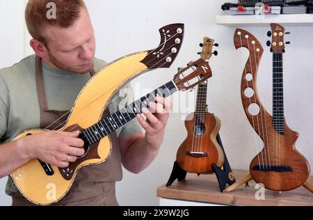 PRODUZIONE - 27 maggio 2024, Sassonia, Lipsia: Nel suo piccolo laboratorio nella parte occidentale di Lipsia, il chitarrista Tom Ziegenspeck canta un ukulele di arpa. Il maestro di 31 anni che produce l'ukulele, particolarmente popolare nelle Hawaii, da 10 anni, è l'unico produttore di ukulele in Germania a costruire un ukulele per gli amanti della musica con quattro corde aggiuntive invece delle solite quattro corde. Suonato elettricamente, il suo esotico suono hawaiano è particolarmente popolare nei gruppi musicali, ma anche nelle Hawaii. L'ukulele, noto anche come pulce saltando alle Hawaii, sta diventando io Foto Stock