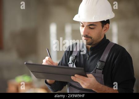 Operaio edile che utilizza un tablet digitale per prendere appunti lavorando in casa Foto Stock