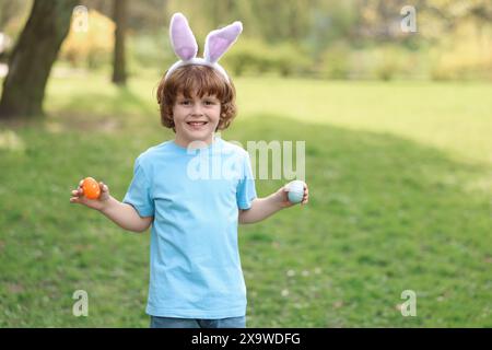 Festa di Pasqua. Bambino carino con orecchie da coniglio che tiene le uova dipinte all'aperto, spazio per il testo Foto Stock