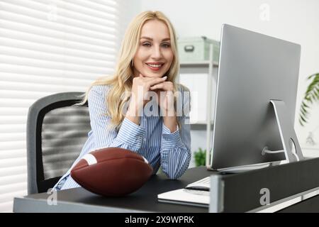 Donna felice con un pallone da football americano a un tavolo in ufficio Foto Stock