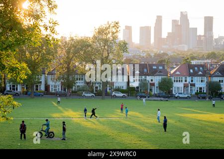I giocatori dilettanti di cricket godono della luce del sole della domenica sera sullo sfondo di uno skyline a sud di Londra di grattacieli a Nine Elms a Battersea, visto da Ruskin Park, uno spazio verde pubblico a Lambeth, il 2 giugno 2024, a Londra, Inghilterra. Foto Stock