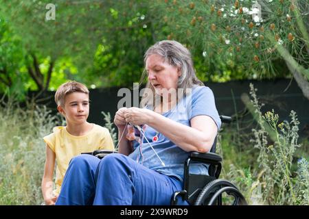 nonna di 65 anni che lavora a maglia all'aperto in compagnia del nipote di 8 anni Foto Stock