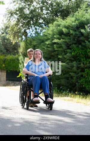 bambino di 8 anni che porta sua nonna su una sedia a rotelle per una passeggiata Foto Stock