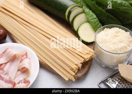 Pasta cruda, pancetta e ingredienti freschi su un tavolo grigio chiaro Foto Stock