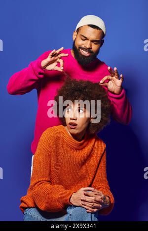 Un giovane uomo e una donna afro-americana, amici, si siedono a stretto contatto in un vivace abbigliamento casual su sfondo blu. Foto Stock