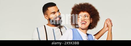 Un uomo e una donna afroamericana, vestiti con stile, si stagliano fianco a fianco su uno sfondo grigio, mostrando il legame di amicizia. Foto Stock