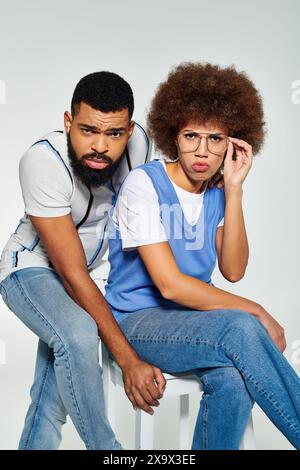 Un uomo e una donna afroamericana in un abbigliamento elegante si posano insieme su uno sfondo grigio, mostrando amicizia e senso della moda. Foto Stock