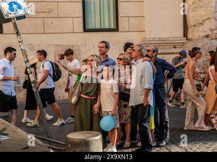 Mentre una donna scatta un selfie di un gruppo di familiari e amici, un ragazzo tira una faccia strana e altri membri del gruppo posano in modi diversi e interessanti. Foto Stock