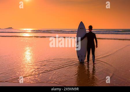 Uno spettacolare tramonto che fiorisce i surfisti sulla Fistral Beach alla fine di uno dei giorni più caldi dell'anno a Newquay in Cornovaglia. Foto Stock