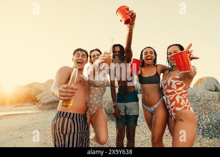 Gruppo di amici che si divertono in spiaggia durante un'avventura estiva, bevendo e godendosi un ambiente all'aperto insieme. Foto Stock
