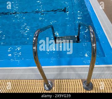 Piscina con scala e acqua. Piscina con corrimano. Scala in acciaio inossidabile nella piscina. Scala con barre di appoggio nella piscina blu Foto Stock