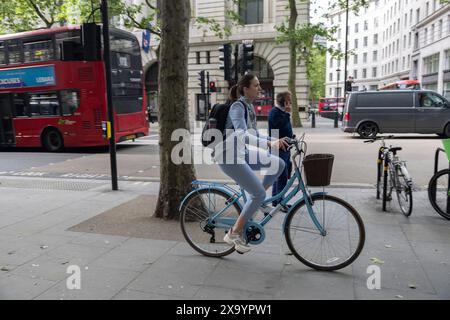 Giovane donna in bicicletta per lavorare lungo il marciapiede pedonale di Aldwych, nel centro di Londra, Inghilterra, Regno Unito Foto Stock