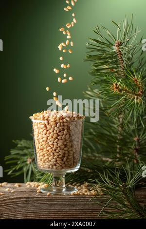 I pinoli vengono versati in un recipiente di vetro. Pinoli sbucciati e ramoscello di cedro su un vecchio tavolo di legno. Copia spazio. Foto Stock