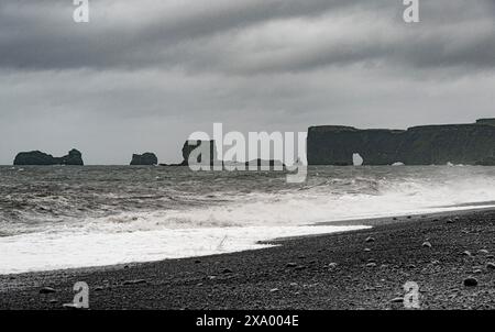 Vik, sabbia nera islandese contro il mare blu profondo, crea una scena accattivante. Il paesaggio vulcanico aggiunge un tocco drammatico Foto Stock