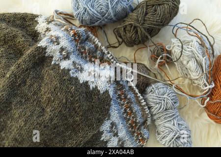 Fotografia piatta di un tradizionale maglione in lopapeysa a maglia islandese in corso sugli aghi con palle in filato di lana Foto Stock