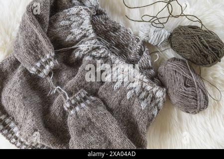 Fotografia piatta di un maglione in lopapeysa a maglia di lana islandese beige in corso sugli aghi con palle di filato Foto Stock