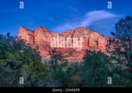 Scenografica montagna rossa che si staglia sul cielo del tramonto con alberi e cespugli sottostanti Foto Stock