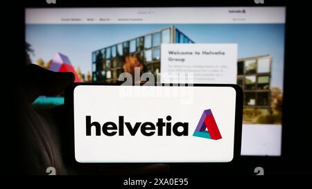 Persona che detiene un cellulare con il logo della compagnia assicurativa svizzera Helvetia Holding AG davanti alla pagina web aziendale. Mettere a fuoco il display del telefono. Foto Stock