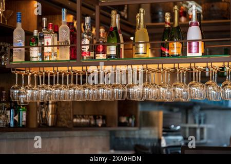 Un bar ben rifornito con numerose bottiglie e bicchieri appesi al contrario Foto Stock