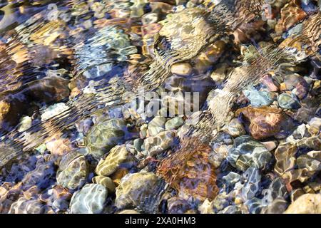 Acqua cristallina che si tuffa su rocce lisce in un ruscello poco profondo Foto Stock