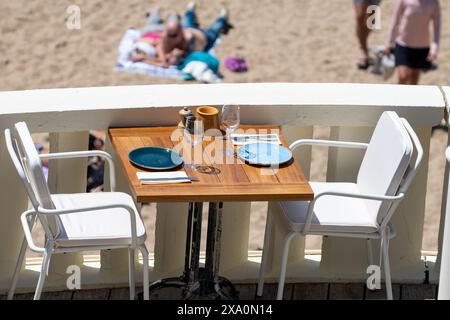 Prima dell'ora di pranzo, un elegante e vuoto caffè sulla spiaggia con tavoli serviti che aspettano gli ospiti nella soleggiata Biarritz, Paesi Baschi, Francia Foto Stock