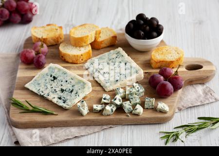 Formaggio blu biologico con uva e olive su tavola di legno, vista laterale. Foto Stock