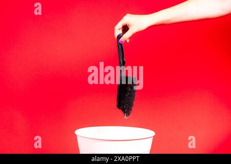 La mano getta la spazzola nel cestino con la confezione su sfondo rosso Foto Stock