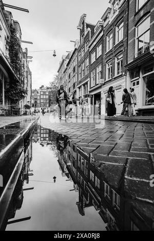 Le case cittadine e un uomo in bicicletta si riflettono in una pozzanghera in una stradina del quartiere Jordaan di Amsterdam, Paesi Bassi, vista il 29 maggio 2024. Foto Stock