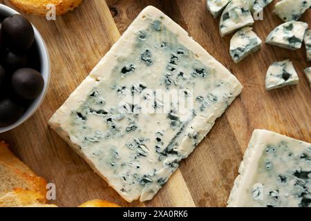 Formaggio blu biologico con uva e olive su una tavola di legno, vista dall'alto. Foto Stock