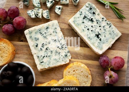 Formaggio blu biologico con uva e olive su una tavola di legno, vista dall'alto. Foto Stock