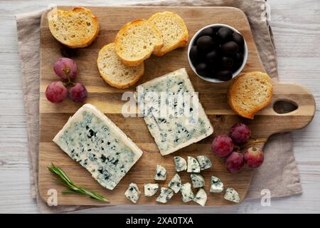 Formaggio blu biologico con uva e olive su una tavola di legno, vista dall'alto. Foto Stock