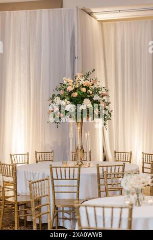 Elegante sala per ricevimenti nuziali in oro e bianco adornata con candele, fiori e tendaggi Foto Stock